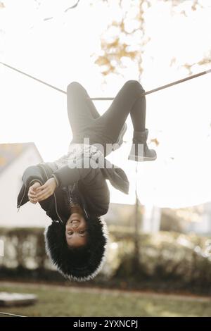 Fille suspendue à l'envers sur une corde de gymnastique à l'aire de jeux Banque D'Images