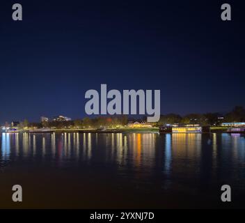 Vue nocturne d'un bord de rivière de la ville avec des lumières colorées se reflétant sur la surface de l'eau calme, créant une scène sereine et pittoresque. Banque D'Images