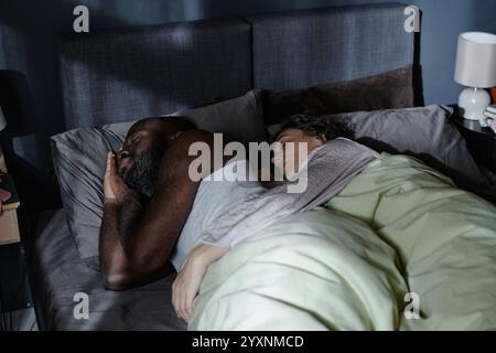 Couple biracial embrassant pendant le sommeil dans le lit la nuit Banque D'Images