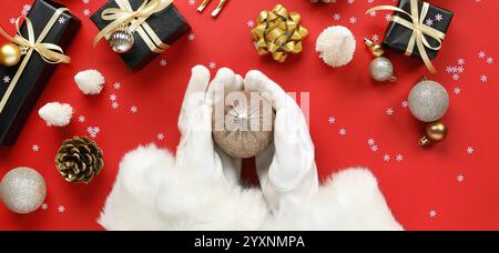 Mains du Père Noël avec de belles décorations de Noël et des cadeaux sur fond rouge, vue de dessus Banque D'Images