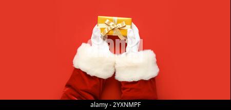 Mains du Père Noël avec cadeau de Noël sur fond rouge, vue de dessus Banque D'Images