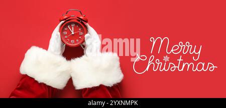 Mains du Père Noël avec réveil sur fond rouge. Bannière pour la célébration de Noël Banque D'Images