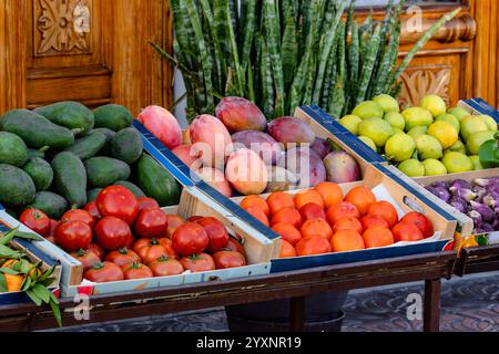 Une table pleine de fruits et légumes frais, y compris des tomates, des oranges et des avocats. Le produit est disposé dans plusieurs boîtes et caisses, et le o Banque D'Images