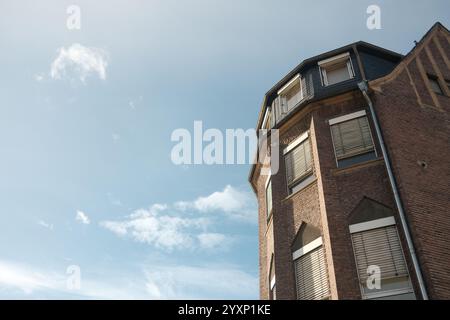 Un bâtiment en briques avec un ciel bleu en arrière-plan. Le bâtiment a beaucoup de fenêtres et un toit incliné Banque D'Images