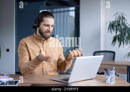 Travailleur masculin dans un environnement professionnel participe à une réunion vidéo en ligne à l'aide d'un ordinateur portable, portant un casque pour la communication. Représente le travail à distance Banque D'Images