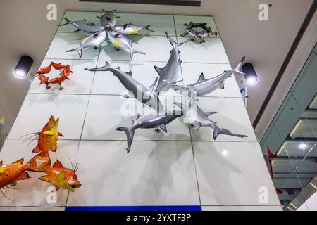 Installation artistique de sculptures colorées de poissons et de requins montées sur un mur carrelé blanc à l'intérieur du terminal de l'aéroport. Banque D'Images