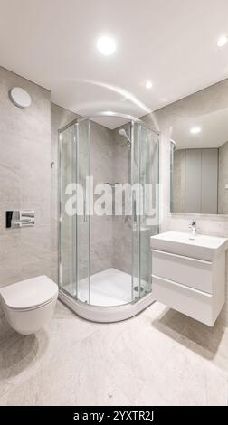 Salle de bains contemporaine avec douche vitrée, lavabo blanc élégant, murs carrelés gris et équipements modernes dans un cadre soigné et minimaliste Banque D'Images