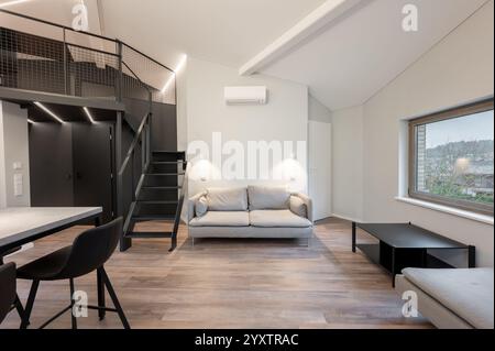 Un appartement loft élégant et contemporain avec une cuisine ouverte avec tabourets de bar, un espace de travail en mezzanine et un design minimaliste épuré. Moderne Banque D'Images