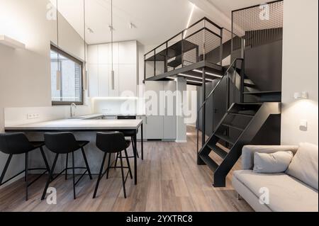 Un appartement loft élégant et contemporain avec une cuisine ouverte avec tabourets de bar, un espace de travail en mezzanine et un design minimaliste épuré. Moderne Banque D'Images