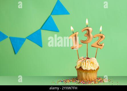 Cupcake d'anniversaire avec numéro 132 bougie - fond vert avec des fanions bleus. Banque D'Images