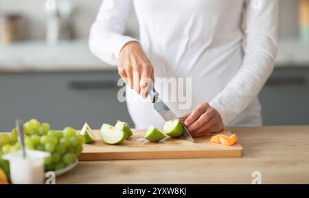 Femme préparant des fruits frais sur une planche à découper en bois dans une cuisine lumineuse Banque D'Images