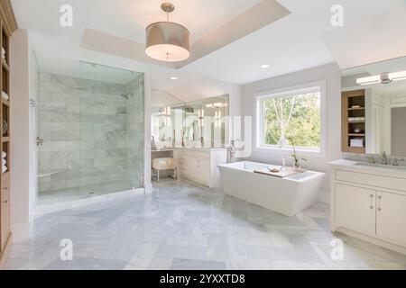Salle de bains principale blanche avec grande baignoire profonde et douche à l'italienne et sol en marbre à motif à chevrons Banque D'Images