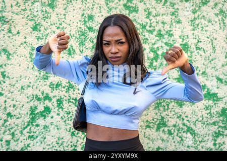 Jeune femme montrant le pouce vers le bas geste exprimant l'aversion et la désapprobation debout sur fond vert Banque D'Images