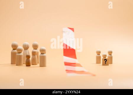 Deux groupes de figures en bois sous la forme de personnes. Un grand groupe et un petit groupe avec un point d'interrogation. Entre eux se trouve un barr rayé rouge et blanc Banque D'Images