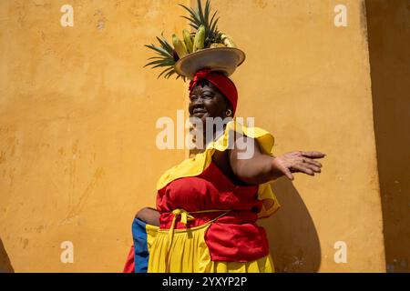 Femme portant Une robe colombienne traditionnelle colorée équilibrant les fruits sur sa tête Banque D'Images