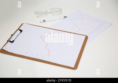 Table de travail de bureau avec rapport de graphiques sur presse-papiers en bois, lunettes et stylo. Banque D'Images