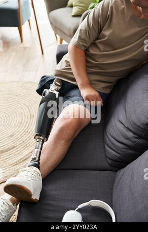 Beau jeune homme est assis confortablement sur un canapé, mettant en valeur sa jambe prothétique tout en se relaxant. Banque D'Images