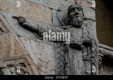 Statue médiévale d'homme pointant du doigt avec une barbe bouclée qui affiche un rouleau avec l'inscription "Ecce Agnus Dei" (Voici l'Agneau de Dieu), à côté de la porte principale, devant l'ouest de la cathédrale de Saint-Georges (Duomo di San Giorgio Martire) à Ferrare, Emilie-Romagne, Italie. Banque D'Images
