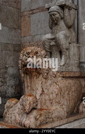 Lion berçant un agneau dans ses pattes et un telamon, sculpté dans les années 1100 À côté de l'entrée principale ouest de la cathédrale Saint-Georges (Duomo di San Giorgio Martire) à Ferrare, Emilie-Romagne, Italie. La partie inférieure de la cathédrale a été construite au XIIe siècle dans un style roman. Banque D'Images