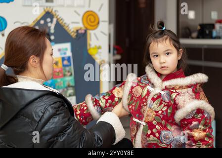 La jeune mère chinoise habille sa fille pour la célébration du nouvel an chinois. Sa fille porte des vêtements traditionnels chinois. Banque D'Images