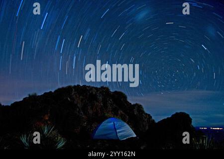 La rotation de la Terre, une photographie longue exposition capture des traînées d'étoiles formant des motifs circulaires dans le ciel nocturne au-dessus d'une tente installée sur un terrain rocheux. Banque D'Images