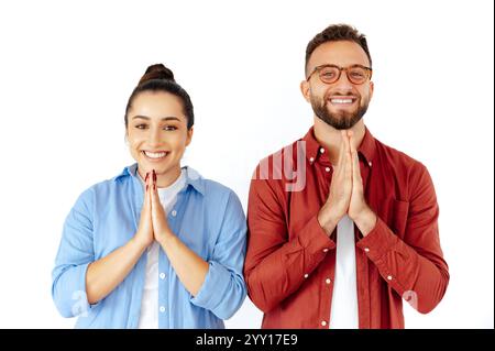 Souriant homme positif et femme avec les mains ensemble dans un geste de prière, exprimant la gratitude ou l'espoir, vêtus de façon désinvolte dans un short, se tiennent sur fond blanc isolé Banque D'Images