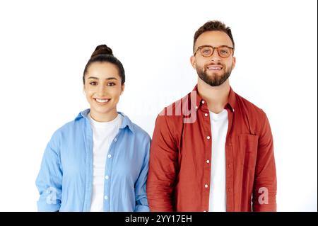 Amicale brune positive homme et femme debout côte à côte sur fond blanc isolé, souriant chaleureusement à la caméra, vêtus de façon décontractée de chemises rouges et bleues Banque D'Images