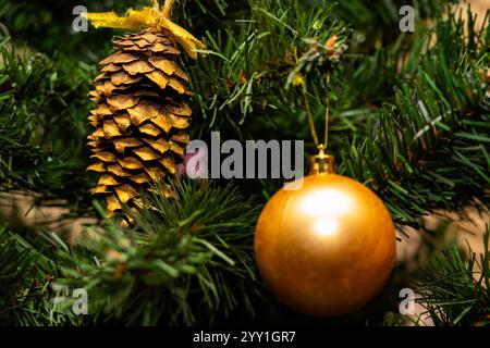 Un sapin de Noël joliment décoré est orné d'une décoration dorée brillante et d'une pomme de pin scintillante. Les aiguilles vertes vibrantes améliorent l'atmo de vacances Banque D'Images
