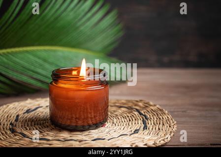 Bougie d'arôme brûlante avec feuille de palmier vert sur fond en bois, espace de copie. Bougie parfumée à la main à la cire de soja, concept de relaxation, modèle confortable. Banque D'Images