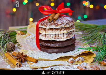Pile de biscuits au pain d'épices glacés et trempés dans le chocolat noués avec un ruban rouge et recouverts de bâtonnets de cannelle. Décorations festives pour les fêtes Banque D'Images