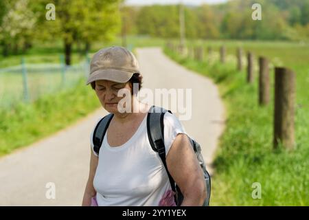 Femme senior marchant sur une route de campagne au printemps, portant une casquette. Concept de voyage à dos actif Banque D'Images