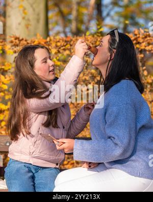 Mère et fille préscolaire mignonne s'amusent ensemble dans la nature dans le parc d'automne, peignent les lèvres avec du rouge à lèvres, se maquillent mutuellement, passent un bon moment à la maison. Banque D'Images