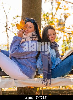 Portrait d'automne de mère avec sa fille. Femme et fille assis dans le parc sur un banc. Mère tient une feuille jaune devant son visage. Amour, relations Banque D'Images