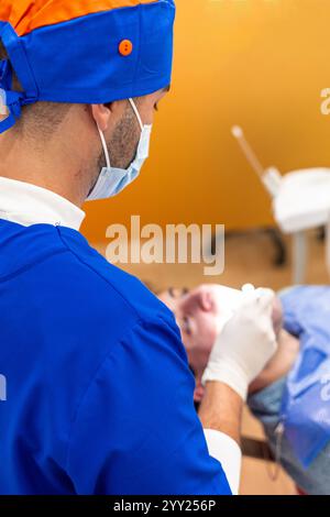 Dentiste portant un masque et des gants effectue une intervention dentaire sur un patient allongé sur un fauteuil dentaire dans une clinique dentaire, à l'aide d'outils professionnels A. Banque D'Images