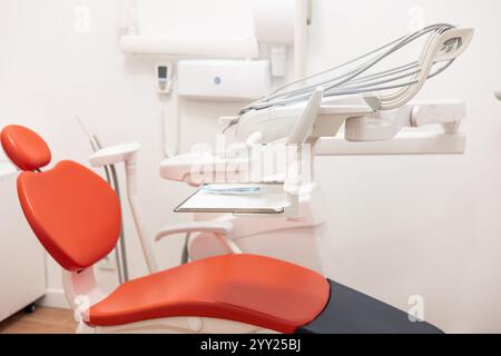 Chaise dentiste rouge vide avec des outils suspendus au-dessus se tient dans le bureau moderne prêt pour le prochain patient montrant bavoir et outils sur le plateau dans une pièce blanche brillante Banque D'Images