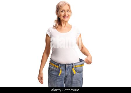 Femme d'âge moyen souriant et essayant sur des jeans, concept de perte de poids isolé sur fond blanc Banque D'Images