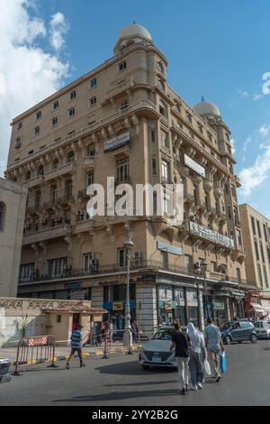 Bâtiment architectural historique avec balcons ornés, toit en forme de dôme et façade beige à Alexandrie, en Égypte, avec des activités de rue et des piétons. Banque D'Images