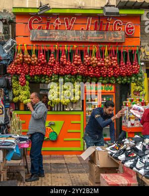 Un stand de jus vibrant à Alexandrie, en Égypte, avec des bananes suspendues, des grenades et des fruits, animé avec les habitants et les vendeurs dans une scène de marché. Banque D'Images