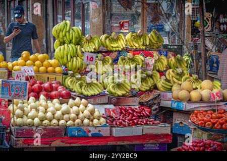Un stand de fruits coloré à Alexandrie, Egypte, affichant des bananes mûres, des poires, des grenades, et des poivrons dans un cadre de marché traditionnel animé. Banque D'Images