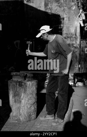 Forgeron au travail à Alexandrie, Egypte, martelant le métal dans un atelier rustique. Un contraste saisissant de lumière et d'ombre met en valeur sa mise au point et son artisanat. Banque D'Images