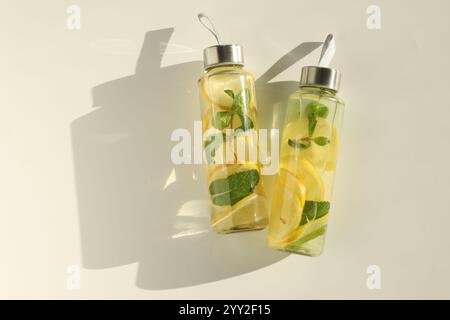 Eau citronnée à la menthe en bouteilles, fruits frais et feuilles sur table blanche, vue de dessus. Espace pour le texte Banque D'Images