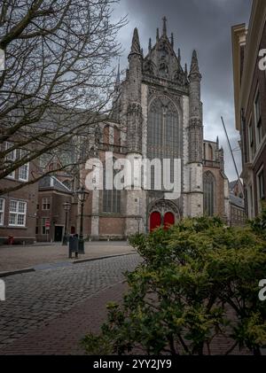 Hooghlandse église de style gothique, Leyde avec de grandes fenêtres complexes et des portes rouges se dresse en évidence au bout d'une rue pavée, entourée Banque D'Images