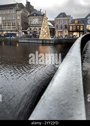 Un arbre de Noël décoré se dresse sur une plate-forme au bord d'un canal, entouré de bâtiments historiques et de boutiques. La scène est vue depuis une rambarde de pont, wit Banque D'Images