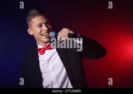 Chanteur talentueux exécutant sur fond sombre avec des lumières de couleur Banque D'Images