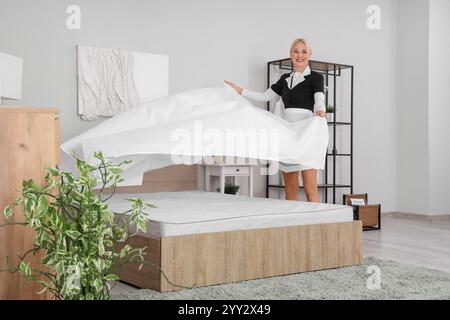 Femme de chambre d'âge moyen faisant lit dans la chambre d'hôtel Banque D'Images
