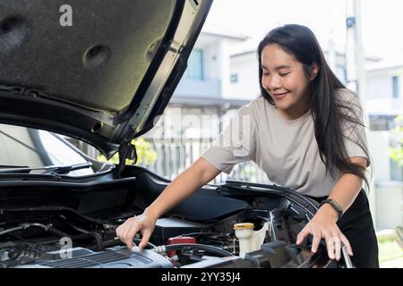 Main de femme vérifier l'huile moteur Une femme sort la jauge pour vérifier le niveau d'huile de sa voiture. Femme réparant la voiture dans le garage ou le travail d'atelier et rep Banque D'Images