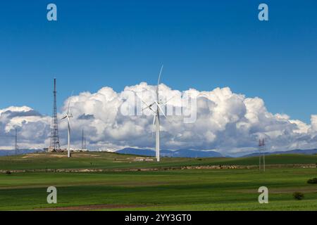 Un paysage géorgien pittoresque avec des éoliennes imposantes au milieu de champs verdoyants sous un ciel bleu vif. Des montagnes enneigées s'élèvent dans la dista Banque D'Images