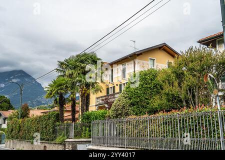 Une charmante villa jaune avec des détails extérieurs ornés, entourée d'une végétation luxuriante, de palmiers et d'une clôture métallique. Sur fond de montagnes Banque D'Images