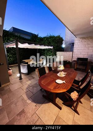 Patio extérieur accueillant avec une table à manger en bois sous un ciel crépusculaire. Des sièges confortables et un décor moderne créent un espace idéal pour les soirées Banque D'Images