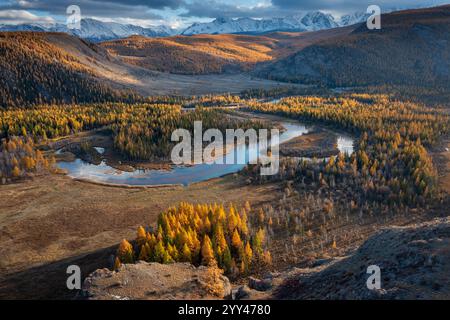 Vue aérienne panoramique du feuillage automnal vibrant, rivière sinueuse, vallée boisée et toile de fond de montagne. Banque D'Images